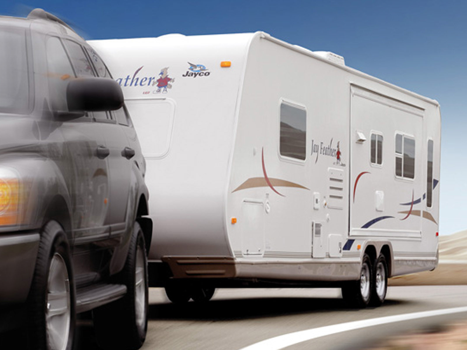 A Jayco “Jay Feather” trailer towed at speed with motion blur, banking through a curve in dramatic light.