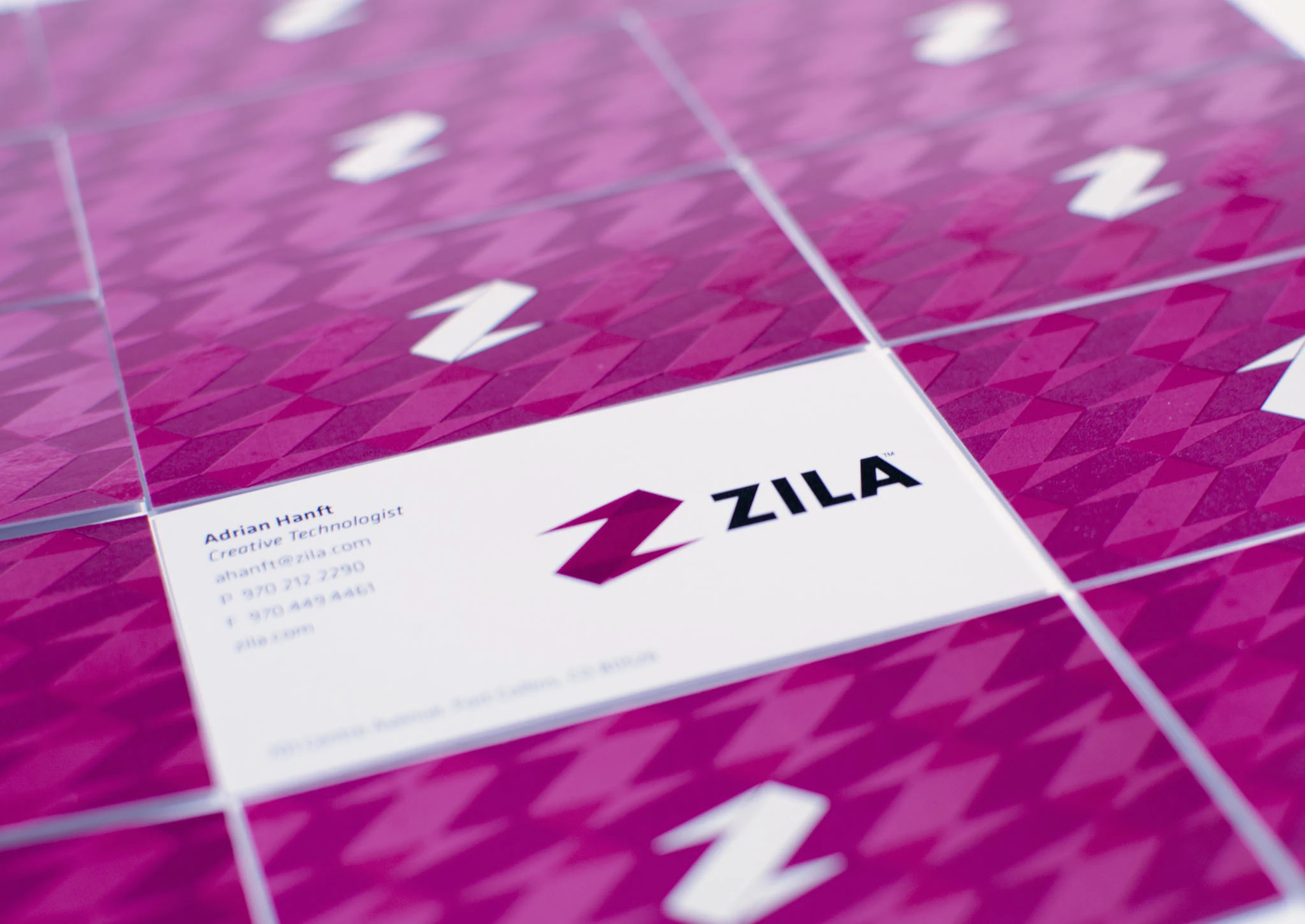 Zila business cards fanned out — a magenta houndstooth pattern built from the angular “Z,” with a clean white card carrying the new ZILA logo.